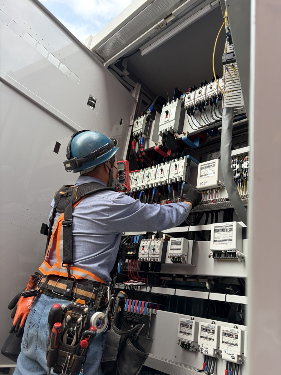 水電雄爸現場施作:身穿橙色安全背心、戴安全帽、配掛工具腰帶,於商業大樓電表暗箱前進行配電盤施作與檢修。