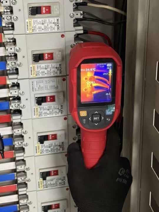 量測檢驗：師傅手持紅外線熱顯像儀掃描分電盤斷路器，畫面顯示最高溫 34.6°C。